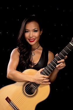 Eine frau mit einer Gitarre vor einem Dunklen Hintergrund