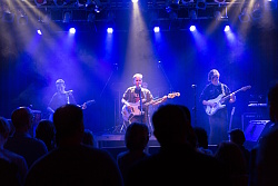 Junge Musizierende auf einer Bühne, mit Gitarren. Sie stehen im Blauen Scheinwerfer Licht.