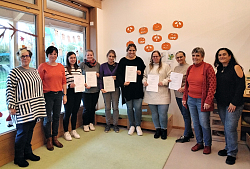 Neun Erzieherinnen stehen zusammen, einige von ihnen halten ein Zertifikat in den Händen.