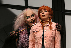 Eine Hexe steht schräg hinter Gretel und bedroht diese.