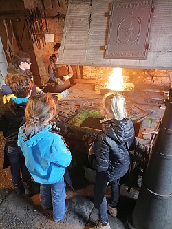 Vorführung in der Hammerschmiede Reichenbach. Kinder stehen im Kreis um einen Tisch auf dem geschmiedet wird.