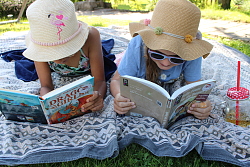 Kinder liegen auf einer Decke im Gras und lesen ein Buch