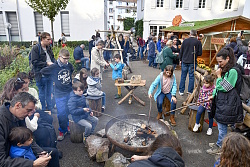 Das Foto zeigt die Waldwerkstatt in der Parkanlage im Rathaus 1.&#13;&#10;Im Vordergrund Kinder, die um eine Feuerstelle sitzen und Stockbrot grillen.