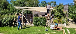 Mehrere Personen errichten auf einer Wiese eine Pergola aus Holz.