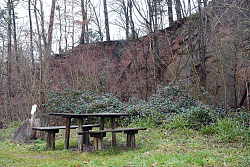 Das Foto zeigt die Sitzgruppe am Wanderparkplatz Altvater, im Hintergrund sieht man die Felswand mit den abgebrochenen dürren Bäumen
