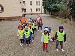 Das Foto zeigt viele Kindergarten Kinder und zwei Erzieherinnen. Sie alle tragen eine Warnweste und sind mit Müllzange und Bollerwagen gerüstet, um Müll einzusammeln.