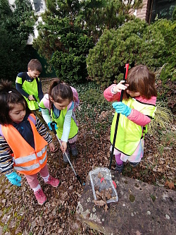 Das Foto zeigt vier Kindergarten Kinder in Warnwesten mit Müllzangen wie sie den Müll aufsammeln.