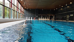 Das Foto zeigt das große Schwimmerbecken im Hallenbad Lahr. Im Hintergrund stehen Liegen am Beckenrand und im Wasser schwimmen  die Besucher.