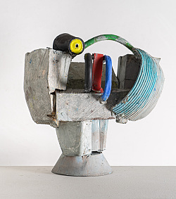 Das Foto zeigt die Skulptur Halber Kopf. Diese ist aus einem halben Eimer, Beton und verschiedenen Griffen zusammengebaut und ist bunt bemalt. 