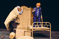 Szenefoto mit dem Sams und Herrn Taschenbier. Das Sams turnt auf einem Bett herum, während Herr Taschenbier in die Bettdecke gewickelt mit dem Zeigefinger schimpft