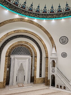 Das Foto zeigt den prunkvollen Saal der Lahrer Ulu Cami Moschee. Die Wände sind mit verschieden Materialien ausgeschmückt und an der Decke lassen sich Wandmalereien erkennen.