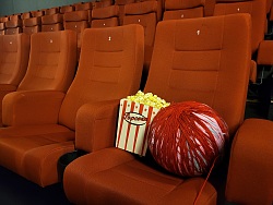 Ein großes Wollknäul und Popcorn stehen auf einem Kinosessel.
