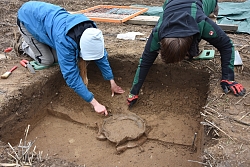 Das Foto zeigt zwei Studenten der Universität Freiburg bei der Freilegung eines Grabes in Diersheim. Im Vordergrund ist die Grube zu sehen.