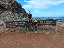 Jonas Volk am Kap der Guten Hoffnung in Südafrika. Im Hintergrund ist das Meer. Er selbst posiert mit seinem Fahrrad an dem Schild ,,Cape of good hope´´.