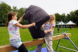 Kinder machen eine Kissenschlacht auf einem Schwebebalken.