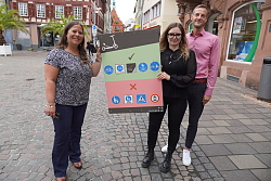 Gruppenbild: Ordnungsamtsleiterin Lucia Vogt, Carina Stuber und Martin Stehr präsentieren das neue Hinweisschild für E-Scooter in der Marktstraße, Altes Rathaus ist im Hintergrund