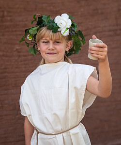 Das Foto zeigt eine festlich bekränzte junge Gallo-Römerin mit einem Becher „Römerlimo“