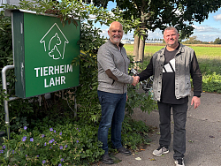 Spirigatis und Jones reichen sich die Hand vor einem Schild mit der Aufschrift &#34;Tierheim Lahr&#34;