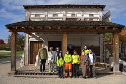 Gruppenfoto vor der Römeranlage (hintere Reihe, von links): Hermann Kleinschmidt, ehrenamtlicher Stellvertreter des Oberbürgermeisters; Dr. Beate Grimmer-Dehn, 1. stellvertretende Vorsitzende der Gesellschaft für Archäologie in Baden-Württemberg e.V.; Silke Höllmüller, FSJler Constantin Berthele; Matti Mielke, Bildungsreferent der Jugendbauhütte Baden-Württemberg.&#13;&#10;Vordere Reihe (von links): FSJlerinnen Anne Herz, Jule Denter und Antonia Bobke; Vera Bregler, Kulturvermittlerin der Römeranlage, sowie Astrid Paul, Ingenieurin, Fachkraft für Lehmbau und Geschäftsführerin der „naterra GbR“ und „LehmKunstWerk“.&#13;&#10;&#13;&#10;