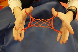 Zwei Hände halten einen dicken, zu einer kunstvollen Figur verflochtenen Faden.