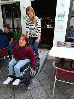 Frau schiebt eine andere Frau im Rollstuhl eine Rampe vor einem Restaurant hinauf