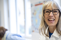 VHS-Programm der VHS Lahr bietet auch Acrylmalkurse - Person in weißem Malkittel steht an einem mit Farbklecksen bedeckten Tisch mit Malutensilien und Papierrolle, im Hintergrund eine weitere Person in blauer Kleidung.