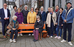 Vertreterinnen des Frauenpolitischen Forums und von Inner Wheel mit Oberbürgermeister Markus Ibert (links) und Fabian Roßmanith (Abteilung Grün und Umwelt) präsentieren die Orangene Bank. Sie stehen um die Bank gruppiert. 