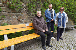 Achim Noefer, Vorsitzender des Lions Club Lahr Schwarzwald, Fabian Roßmanith, Abteilungsleiter Grün und Umwelt, und Petra Bredemeyer, Präsidentin des Lions Club Lahr Schwarzwald, freuen sich über die neue Seniorenbank an der Stadtmühle, gespendet vom Förderverein Lions Club Lahr Schwarzwald. Sie sitzen und stehen auf und neben der Seniorenbank an der Stadtmauer.