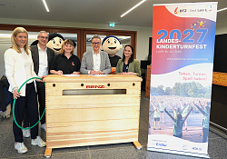 OB Markus Ibert unterzeichnet den Vertrag auf einem Turnkasten. Um ihn stehen die Verantwortlichen des Badischen Turnerbundes und die Maskottchen des Kinderturnfestes. 