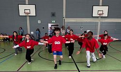 Auf dem Bild sind einheitlich angezogene Kinder, die eine Tanzeinlage vorführen in einer Turnhalle