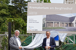 Auf dem Bild sind zwei Männer zusehen wie sie ein Bauschild enthüllen.