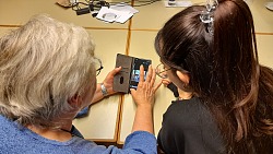Das Foto zeigt eine Schülerin, die eine Besucherin beim Umgang mit ihrem Smartphone unterstützt