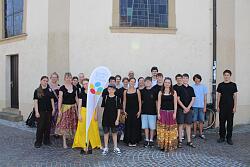 Gruppe von Menschen unterschiedlichen Alters steht vor einem hellen Gebäude mit zwei Fenstern und einem Banner mit der Aufschrift &#39;landes musik festival&#39;