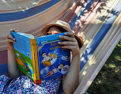 Das Foto zeigt ein Mädchen in der Hängematte liegend beim Lesen