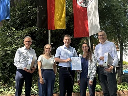 Gruppenbild von links Markus Ibert, Oberbürgermeister Stadt Lahr; Katharina Tränkle, Amt für Gewerbeaufsicht und Immissionsschutz; Nikolas Stoermer, Erster Landesbeamter; Teresa Frenssen, Projektleiterin E-Werk Mittelbaden; Bernhard Palm, Vorstandsvorsitzender E-Werk Mittelbaden vor wehenden Fahnen beim Landratsamt Offenburg. &#13;&#10;&#13;&#10;