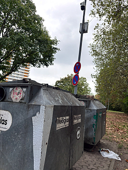 zwei Glascontainer, dahinter ein Laternenpfahl auf dem oben ein Videoschutz angebracht ist. 