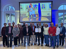 Gruppenbild mit Lahrs Oberbürgermeister Markus Ibert (mit Amtskette), Kaluschs Bürgermeister Andrii Naida (auf der Leinwand) und Mitglieder des Lahrer Gemeinderats präsentieren die unterzeichneten Partnerschaftsurkunden.