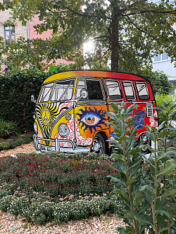 Ein VW-Bulli mit knalligen Farben und verrückte Designs. Hinter dem Bulli kann man durch einer der Fenster den Kopf rausstrecken. Ein perfekter Fotopoint für schöne Erinnerungen.