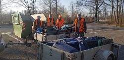 Vier Jäger, in Warnwesten gekleidet, stehen zwischen einem Container und zwei mit Müll beladenen Anhängern