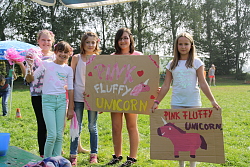 Das Bild zeigt fünf Mädchen, die rosa-weiße Puschel und Pappschilder mit der Aufschrift Pink Fluffy Unicorn und einer Zeichnung des Einhorns hochhalten.