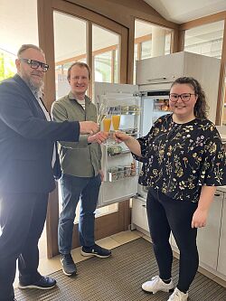 (Von rechts) Die Ideengeberin Elke Ablietz, der Ehrenamtliche Maximilian Rusch und EBM Guido Schöneboom  vor dem geöffneten Öffentlichen Kühlschrank stoßen 2024 mit Sekt auf die Eröffnung an