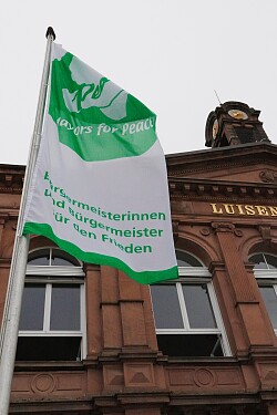 Flagge Mayor for Peace flattert vor der alten Luisenschule imm Wind