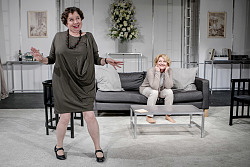 Saskia Vester sitzt verträumt auf einem Sofa im Wohnzimmer. Vor ihr steht Franziska Traub mit einem Lächeln im Gesicht. 