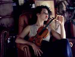 Die Violinistin Alena Baeva sitzt in einem Sessel und hält eine Violine an sich.