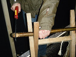 Das Bild zeigt Hände, die einen in einem Holzbock liegenden dünnen Stamm absägen.