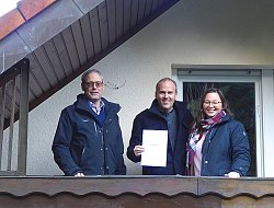 Christian Dunker von der Ortenauer Energieagentur (links), Michael Vehrenkamp (Mitte) und die Lahrer Klimaschutzmanagerin Madeleine Meinhardt stehen auf dem Balkon eines Hauses. Michael Vehrenkamp zeigt seine Urkunde für die 50. Energieberatung in die Kamera.