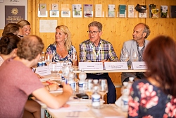 Mehrere Personen sitzen um eine U-förmige Tischgruppe drum herum und diskutieren.