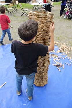 Das Bild zeigt einen Jungen von hinten, der einen runden Turm aus kleinen Klötzchen baut, der schon höher ist, wie er selbst. 