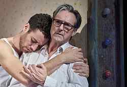 Ein Junger Mann umarmt einen äteren Mann, dessen Blick als verzweifelt oder traurig interpretiert werden kann.