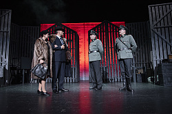 Szenenausschnitt: Links im Bild stehen ein Mann und eine Frau, beide tragen Pelz. Rechts im Bild stehen zwei Schauspieler als Offiziere des Nationalsozialistischen Regimes mit Uniformen aus dem Jahre 1945.